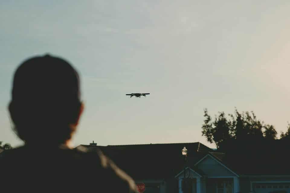 Man in Silhouette Watching Quadcopter Drone in the Air Over House